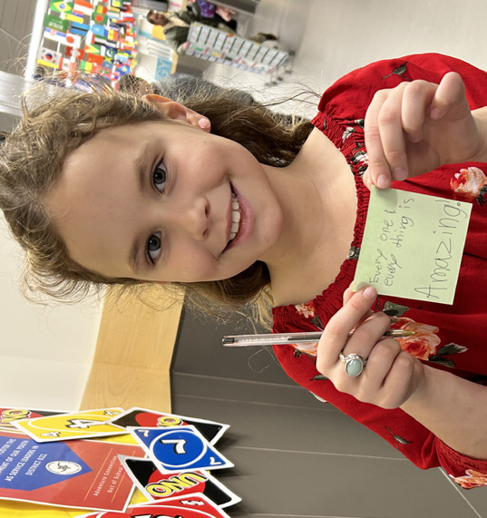 A young girl smiling and holding up a small card she made.