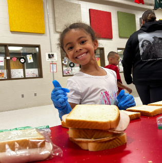 A young girl holding a sandwich she prepared.