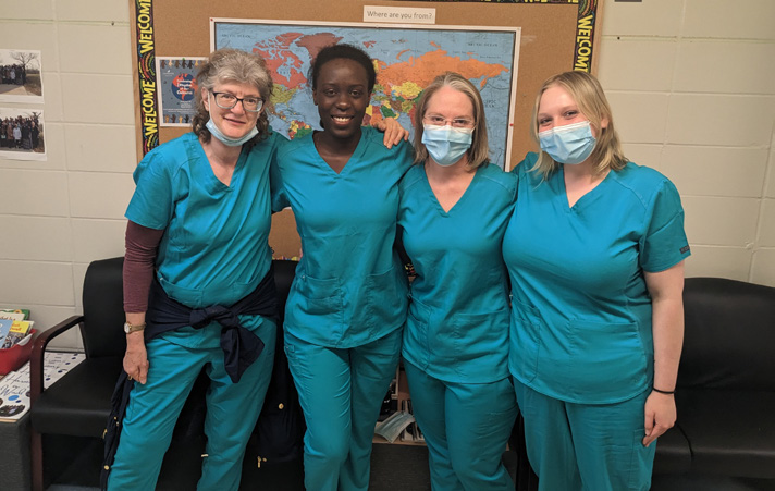 Four healthcare professionals in blue scrubs smiling together