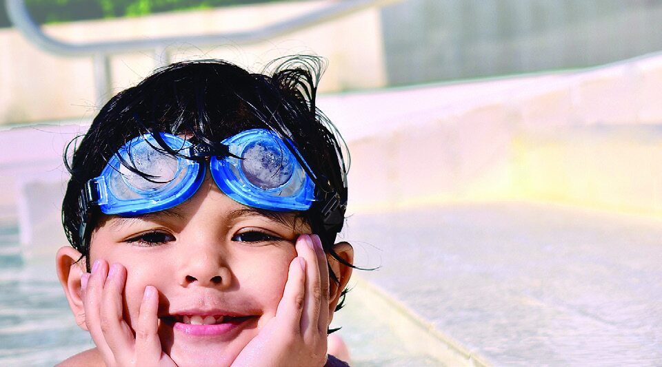 Child wearing blue swimming goggles smiling in the water