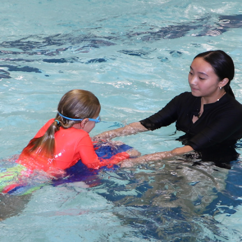 A swimming instructor helping a young student practice with a kickboard