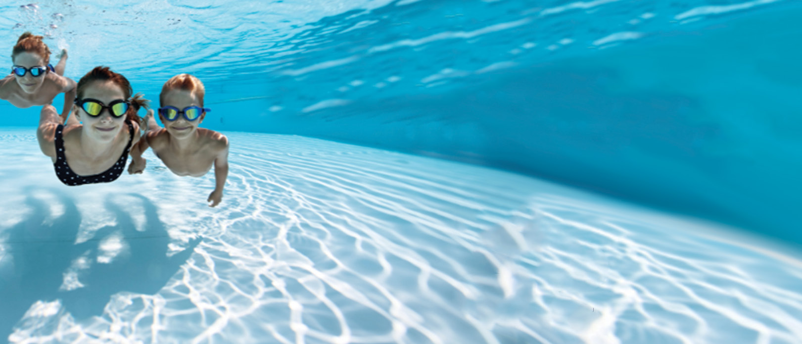 Three children wearing goggles in a swimming pool