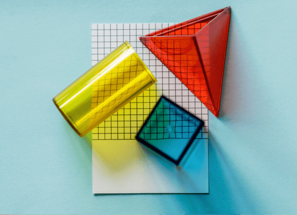 A set of colorful 3D geometric shapes including a yellow cylinder, a red pyramid, and a blue cube on a grid background