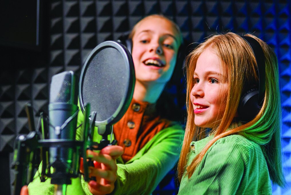 Two girls wearing headphones and singing into studio microphones