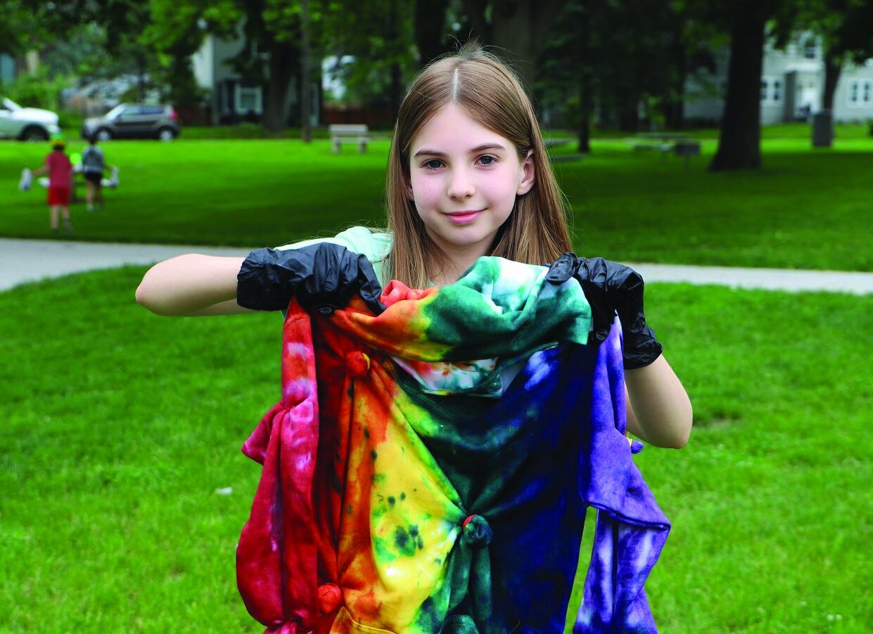 A young girl smiling while wearing a colorful tie-dyed shirt
