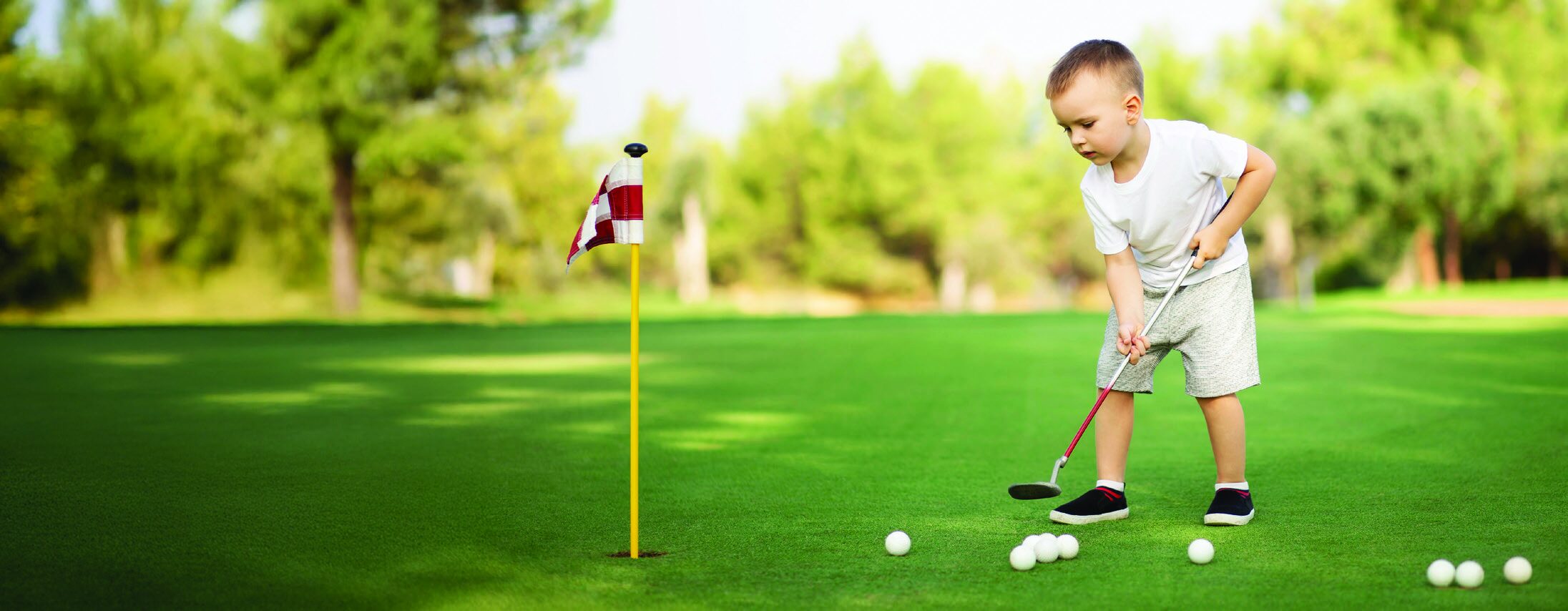 A young boy practicing golf on a green with a flag