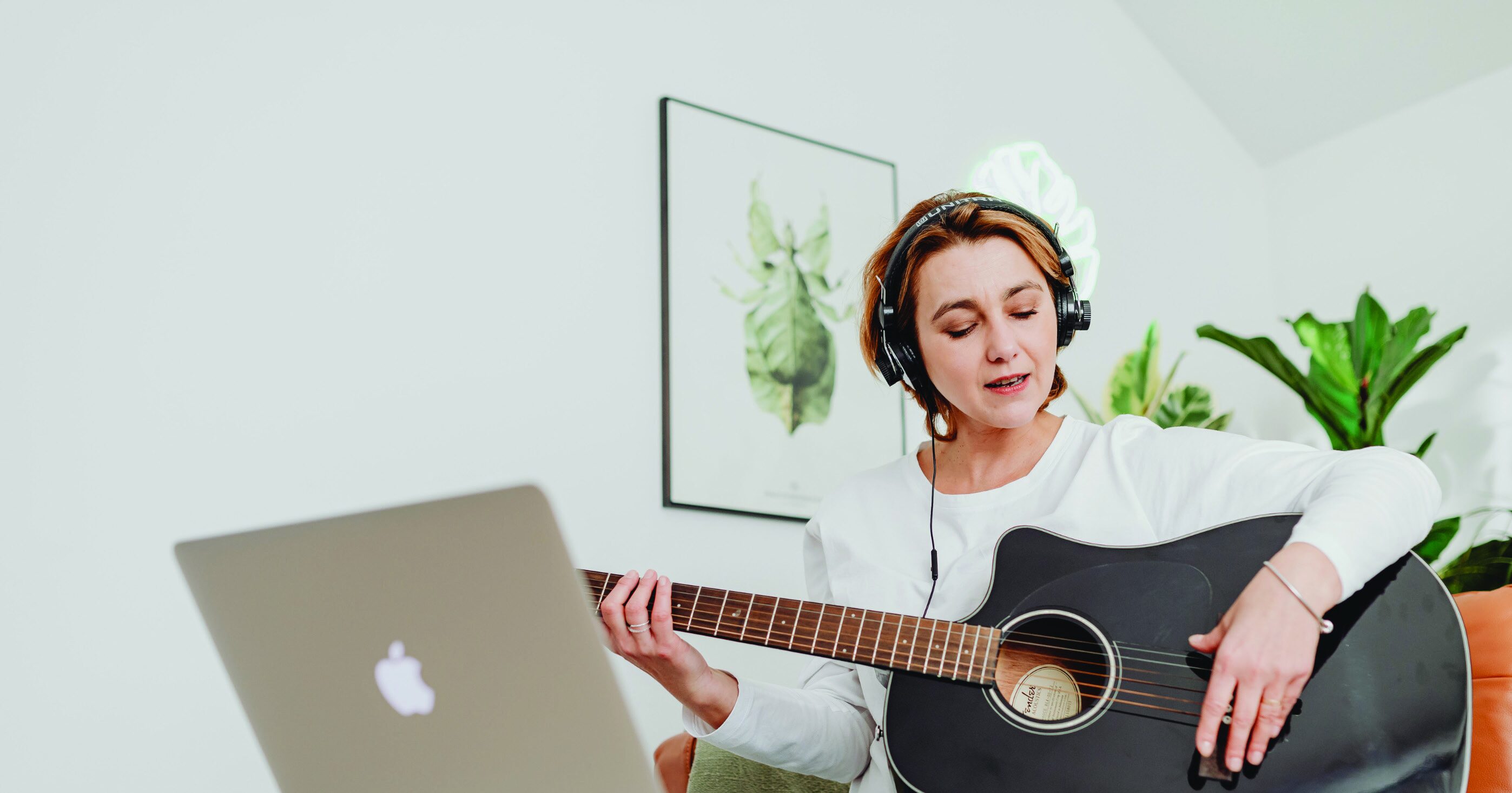 Woman with headphones and guitar looking at a laptop for an online music course