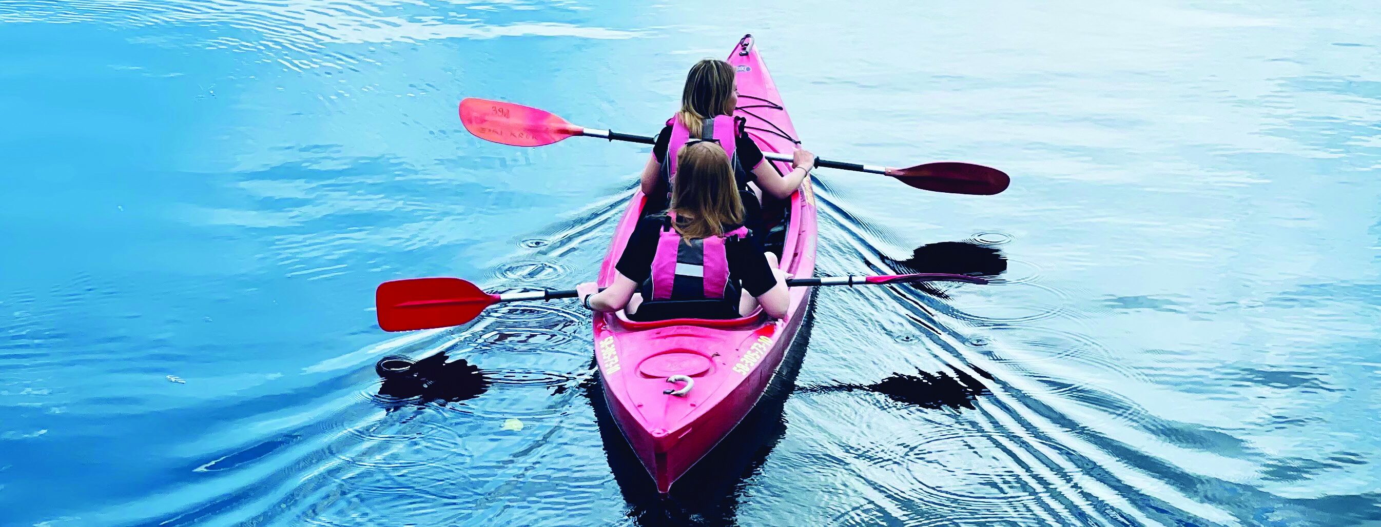 Two people in a pink kayak paddling across calm blue water.