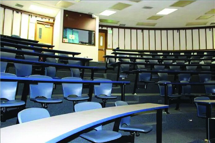 A tiered lecture-style classroom with blue chairs and white tables.