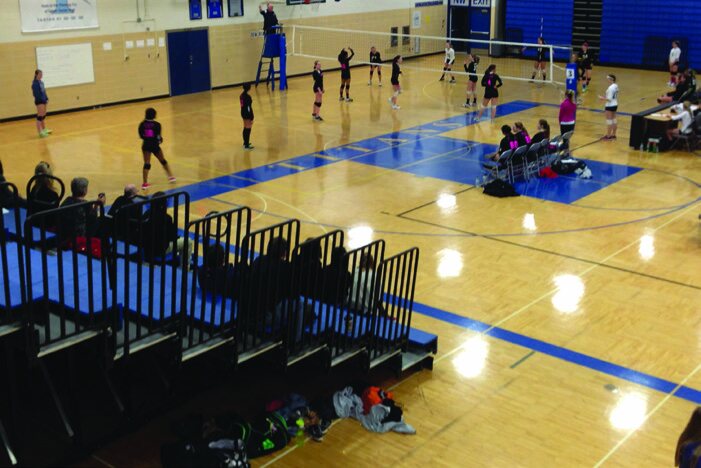 A large indoor gymnasium with basketball hoops and volleyball nets.