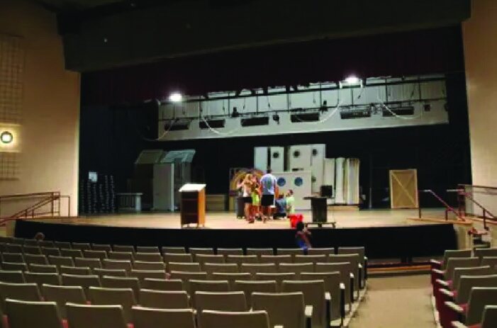 A school auditorium stage with theater seating in the foreground.