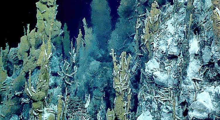 Blue-green underwater scene of hydrothermal vent chimneys and mineral formations on the seafloor