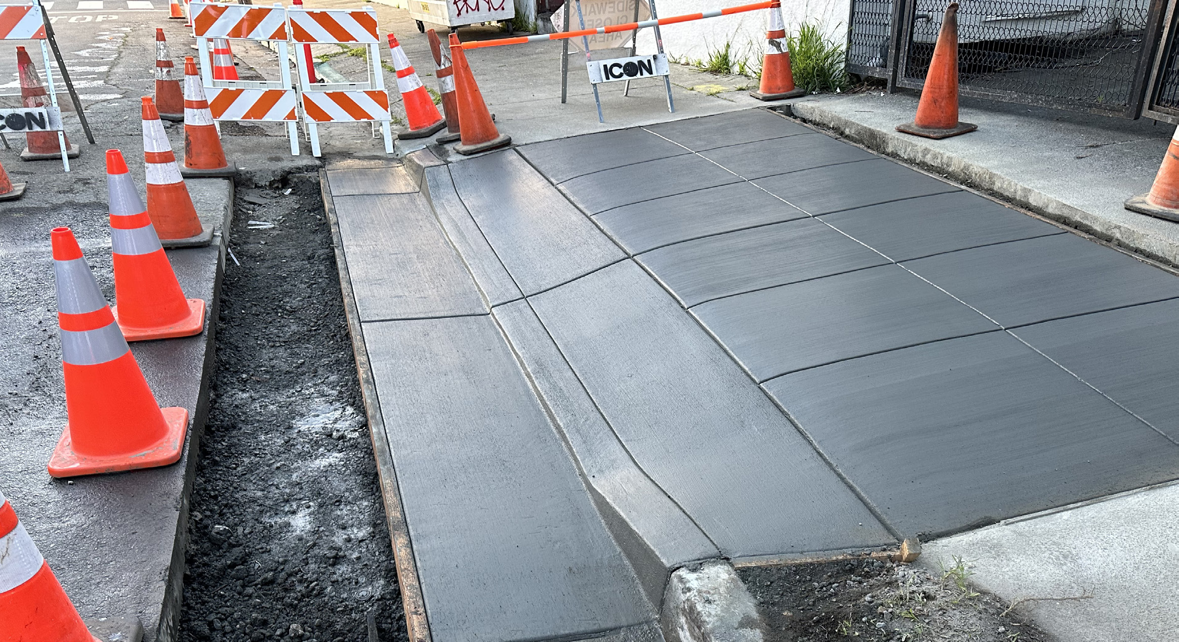 Commercial concrete driveway entrance under construction with safety cones