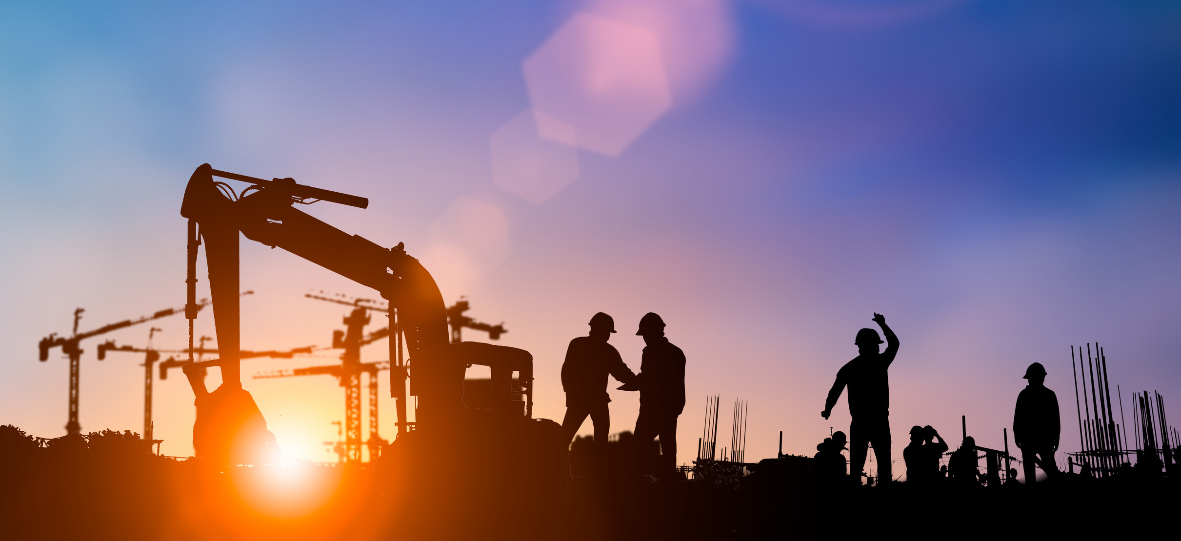 Construction site at sunset with workers and cranes