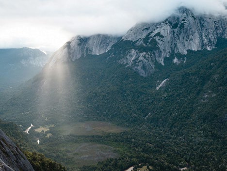 Protected mountain valley with sunlight streaming through dramatic peaks and clouds