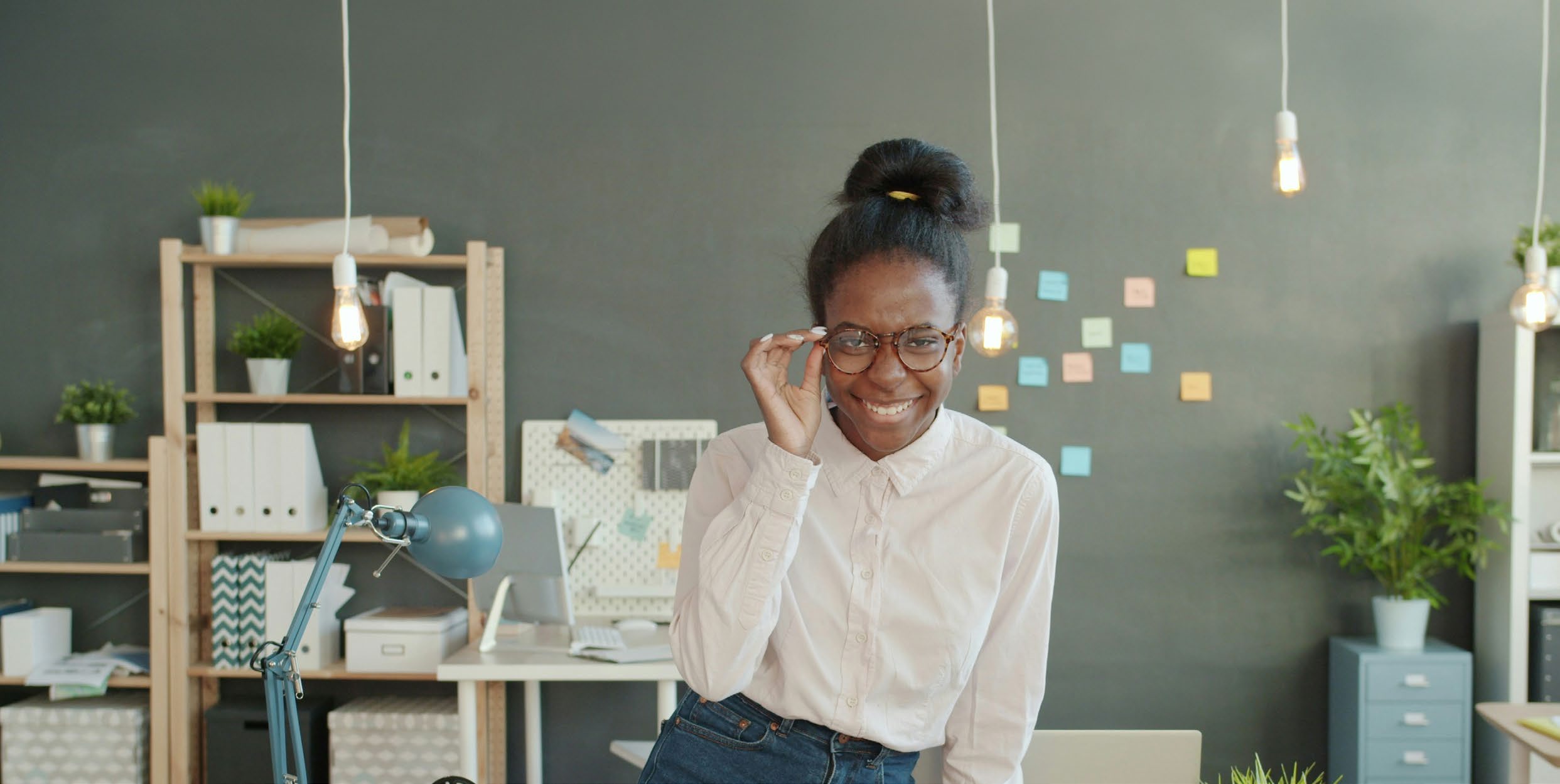 A young black woman with a bun and glasses smiling in a modern office environment