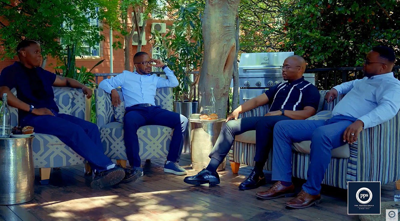 A group of men sitting outdoors on a sofa, having a discussion.