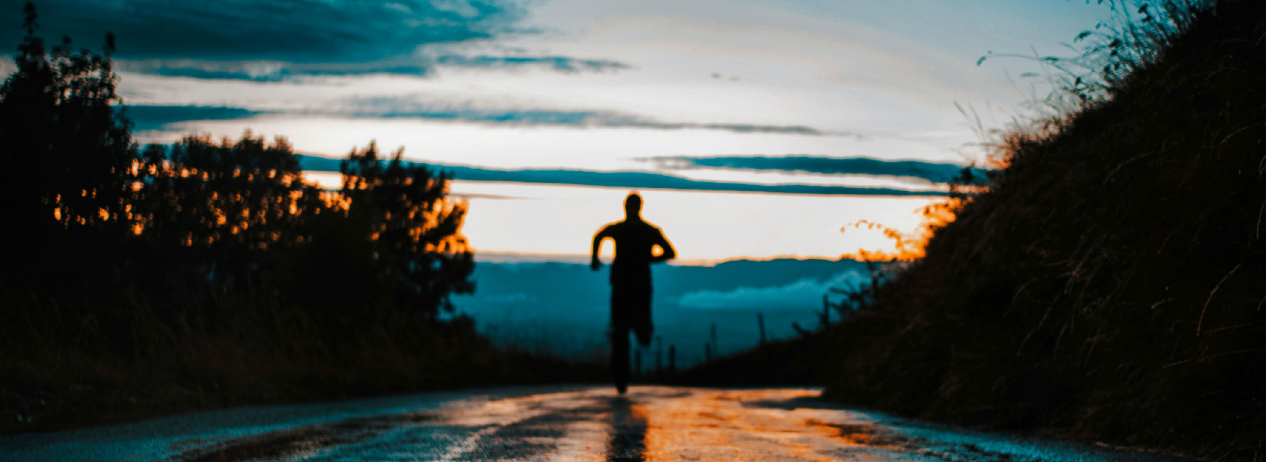 A silhouette of a person running on a coastal road during sunrise