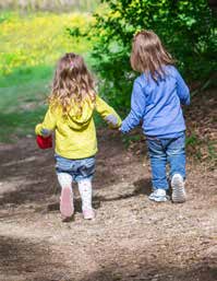 Three children walking outdoors on a trail, backs to camera, surrounded by greenery, representing friendship.