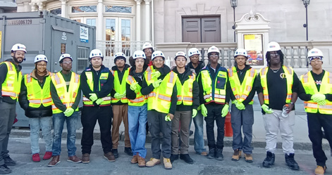 A group of students and professionals in safety gear posing at a construction site.