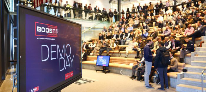 A large group of attendees and a presentation screen at the Suffolk Technologies BOOST Demo Day event