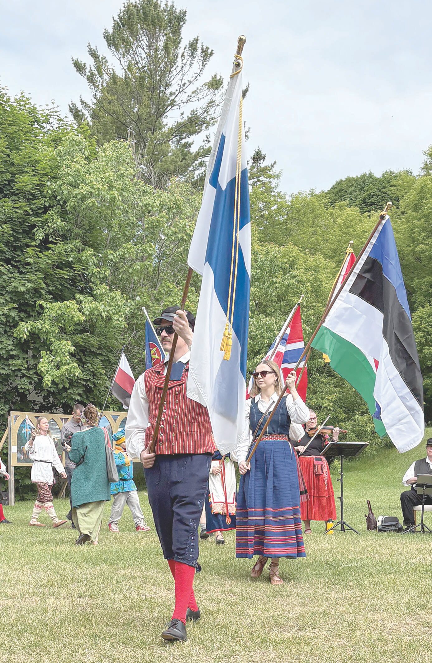 A man in traditional Finnish dress leads a procession with a large Finnish flag