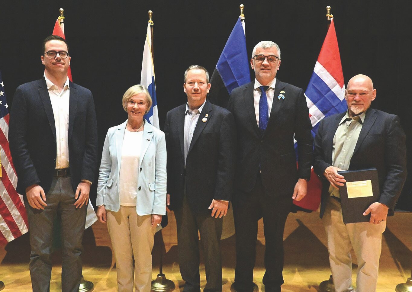 Five people standing together in front of various national flags