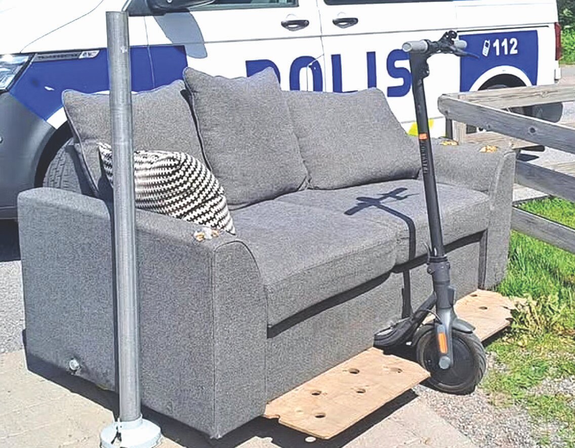 A photograph showing an electric scooter modified with a wooden platform to carry a grey sofa.