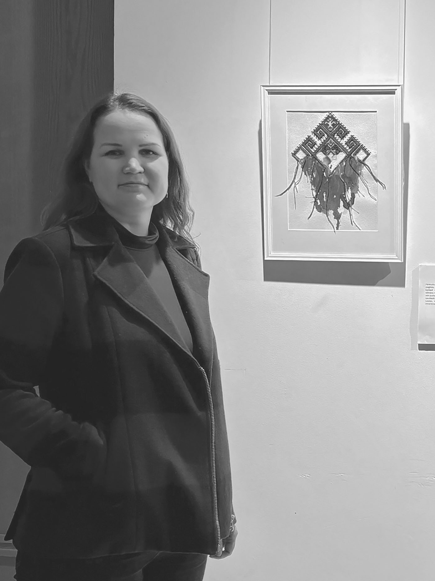 Mari artist Zhanna Toht standing in an art gallery next to a piece of her watercolor and embroidery work.