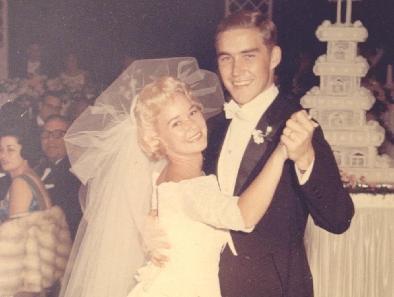 A vintage photograph of a young Alpo and Marjorie dancing at their wedding; a large multi-tiered wedding cake is visible in the background along with other guests.
