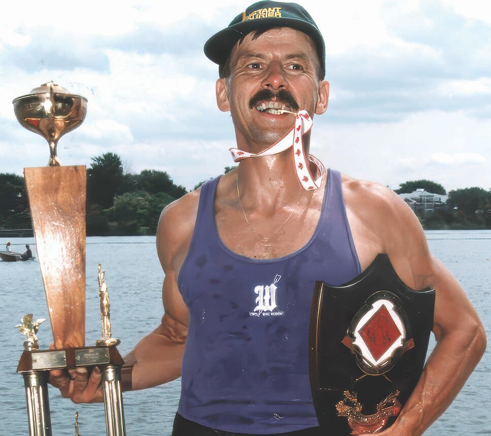 Kari Juurakko standing by water holding trophies and wearing a medal