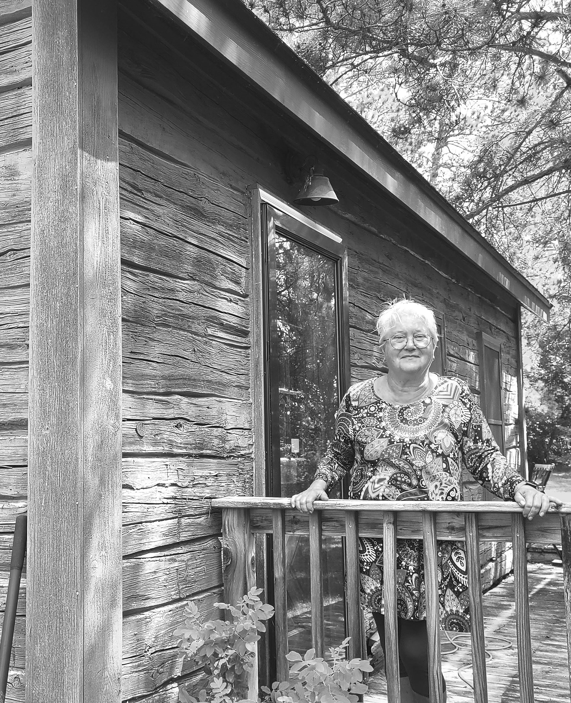 Artist Mary Erickson standing on a deck in front of a Finnish log house.