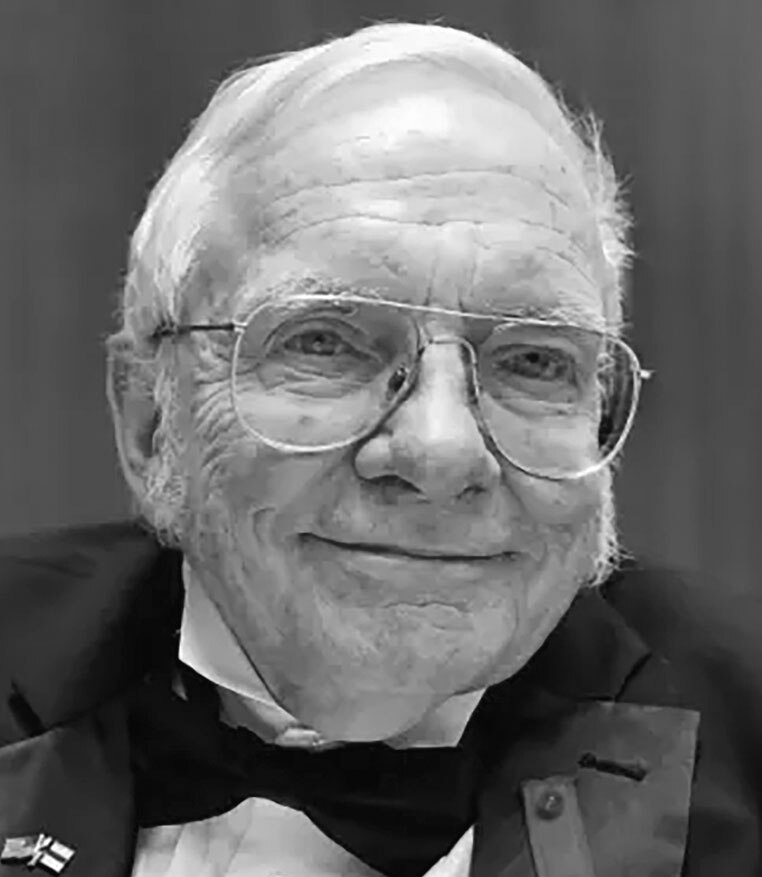Black-and-white portrait of John Oscar Kiltinen wearing glasses and a tuxedo, smiling.