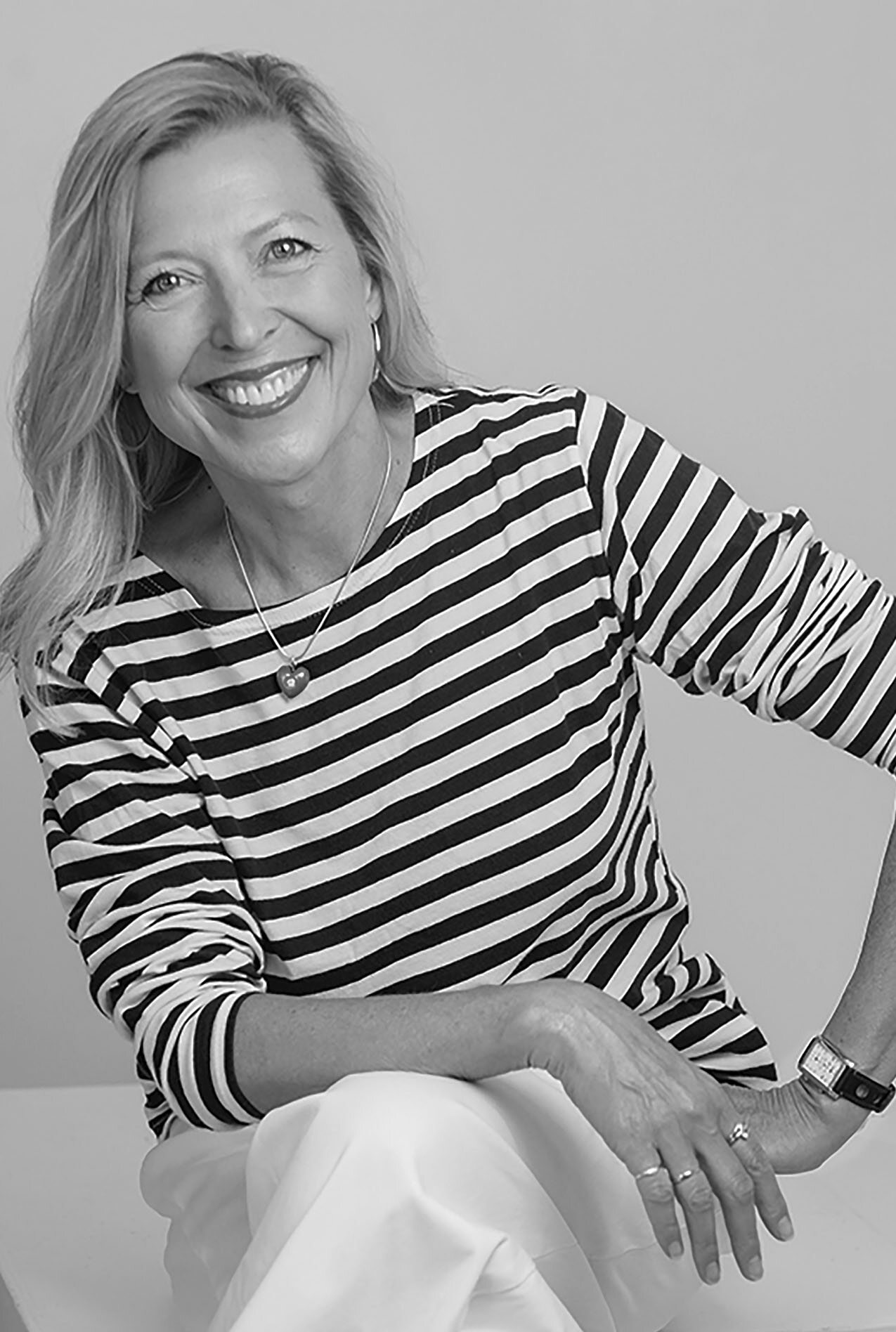 Portrait of a smiling woman wearing a striped top, seated with her hands visible.