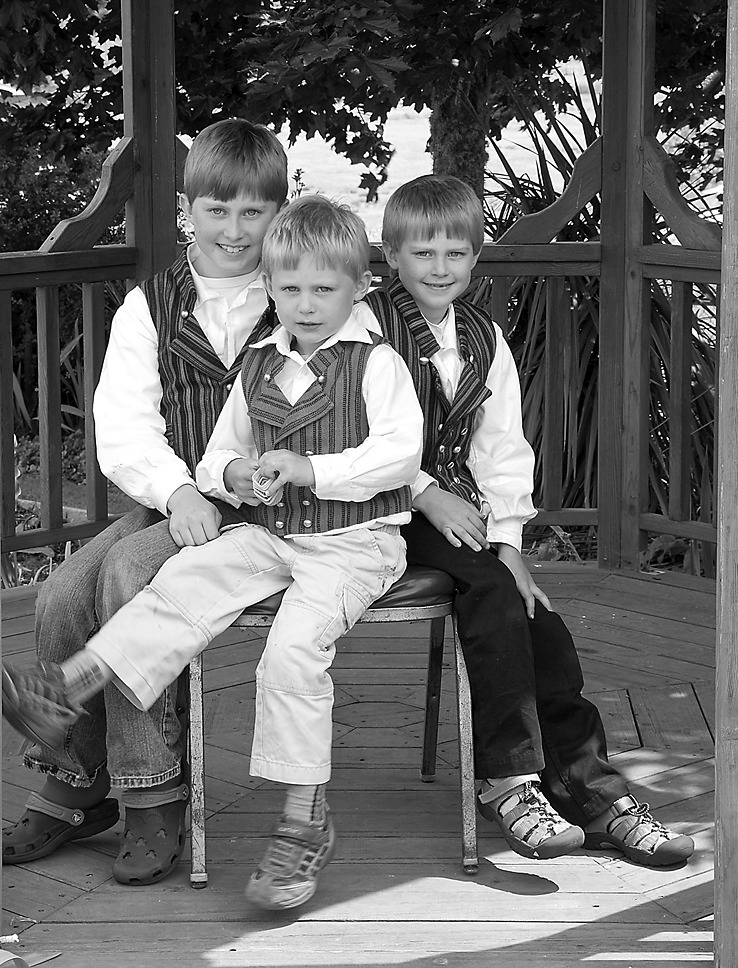 Black-and-white photograph of three young boys sitting together on a wooden bench