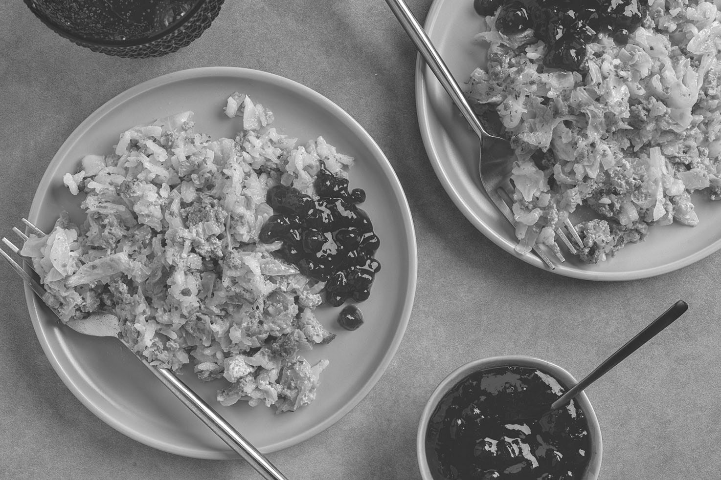 Top-down view of two plates of cabbage casserole with a small bowl of lingonberry jam and a spoon