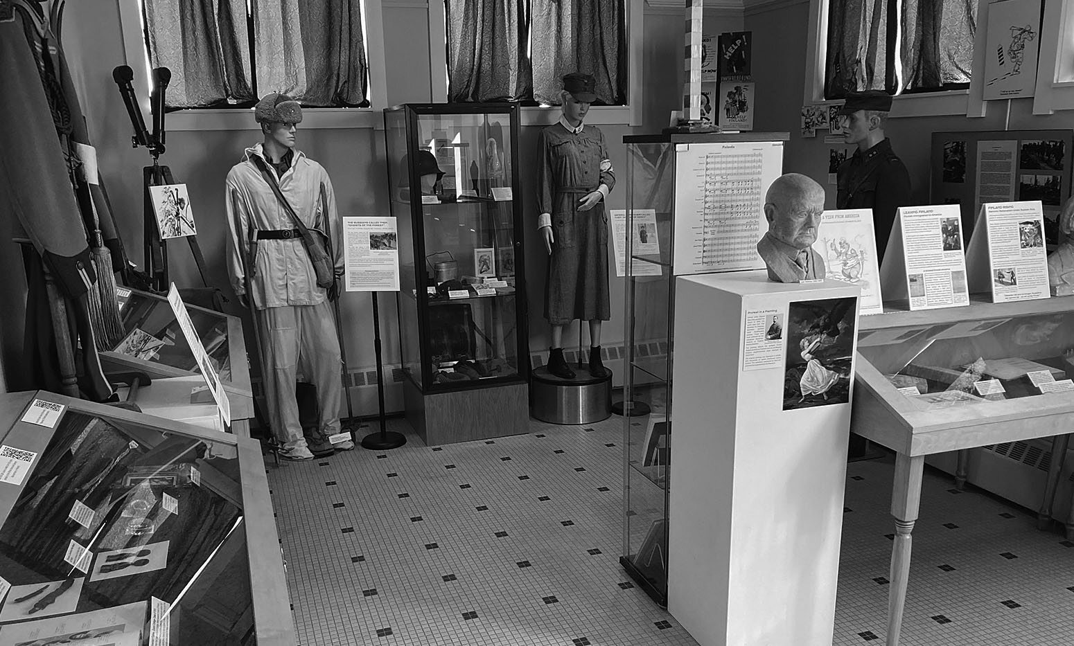 The 'Price of Freedom' museum exhibit at the Finnish American Heritage Center featuring historical military uniforms and glass display cases.