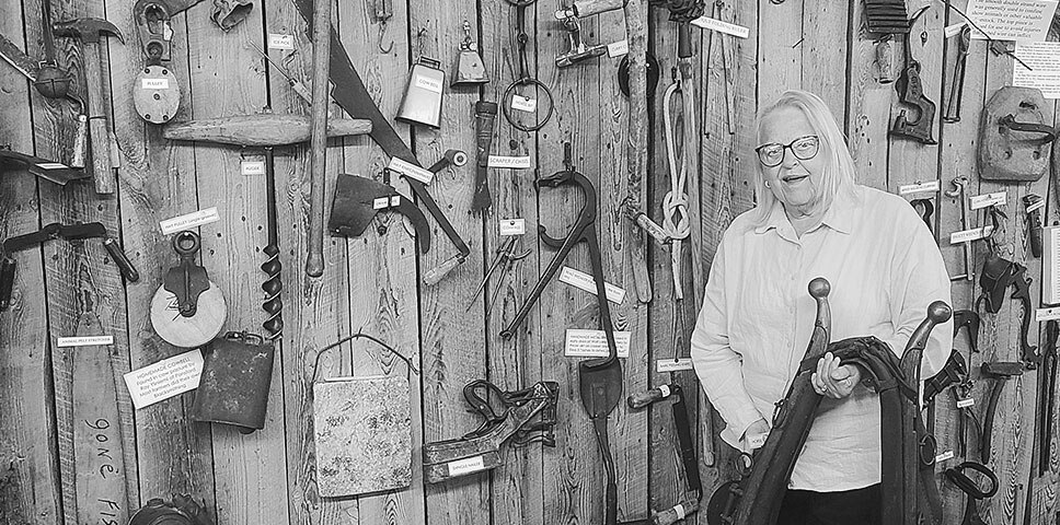 President Gloria Markkula standing in front of a wall of vintage farm and logging tools at the Menahga Historical Museum.