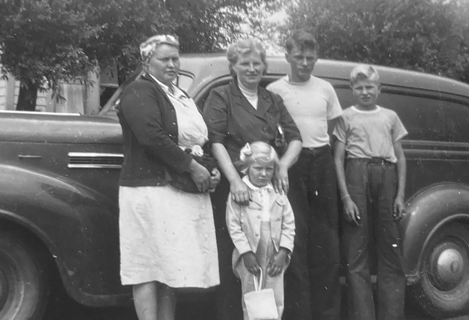Five people posed beside a 1939 Plymouth panel delivery van &mdash; two adult women, two boys, and a young girl.