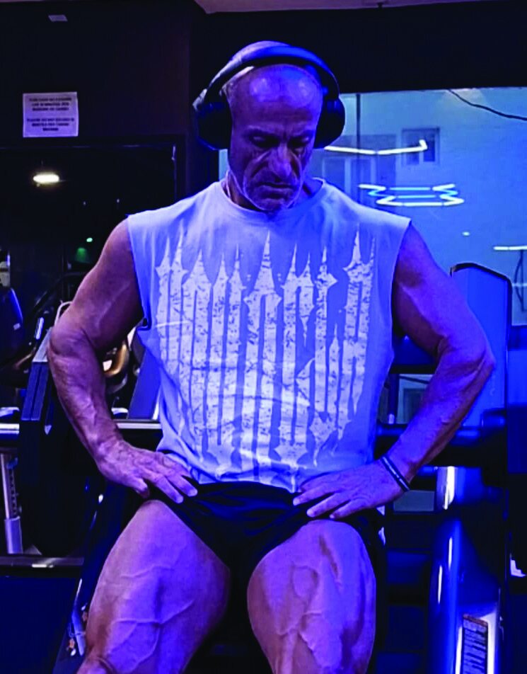 Leonard Torreblanca seated in a gym, wearing headphones and a sleeveless shirt, hands on thighs