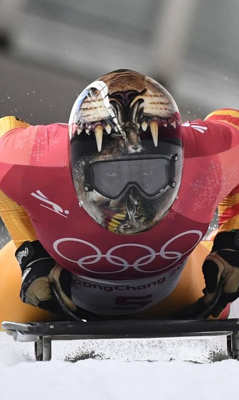 Close-up action photo of a skeleton racer on the track with Olympic rings